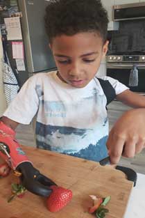 A boy with his machined left hand trying to hold a strawberry