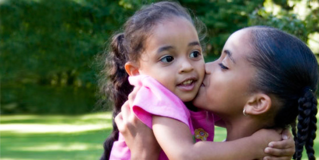 Young woman holding up a little girl and kissing her on the cheek.