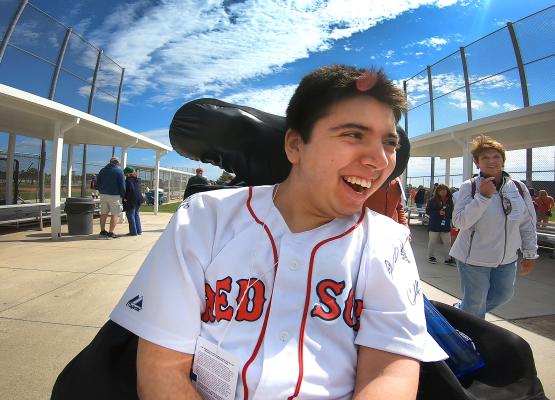 Young man with dark hair in Red Sox shirt smiles in wheelchair