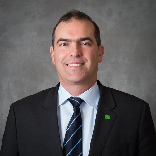 Man with dark hair wearing a black blazer, white shirt, and a blue-striped tie.