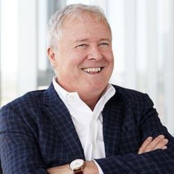 Man with white hair wearing a blue plaid blazer and a white shirt.