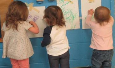 Three children colouring on paper on the wall.