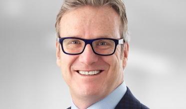 Man with light hair wearing blue glasses, a dark blue blazer and a light blue shirt