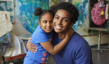 A teenager giving hug to a sibling with a background of some colourful drawing