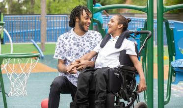Two adults playing basketball, one of them is on wheelchair