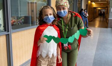 An adult with mask on, taking a photo with child with mask on