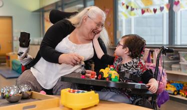 An senior is facing a young child, who is in a wheelchair