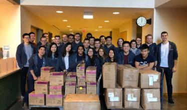 A group of adults taking group photo, with some carton boxes in front of them