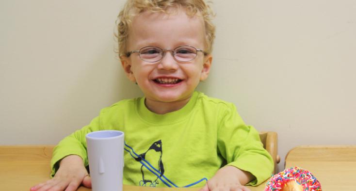 Boy at table with cup and donut.