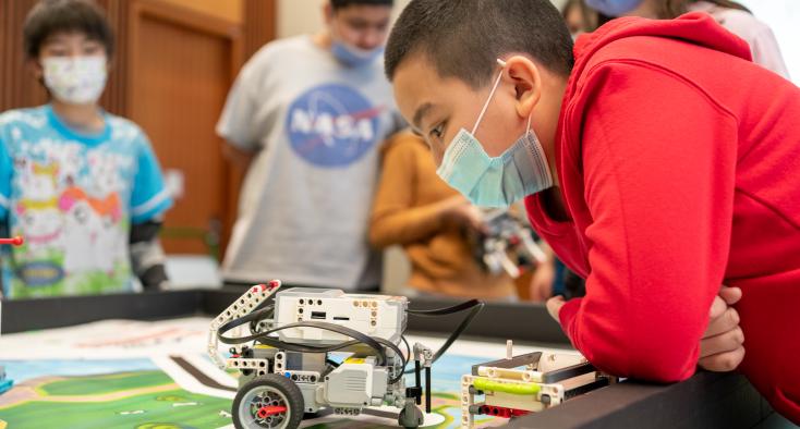 boy with black hair leaning over his robot