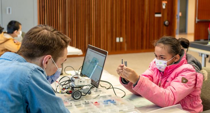 girl at a table with a volunteer working on a robot