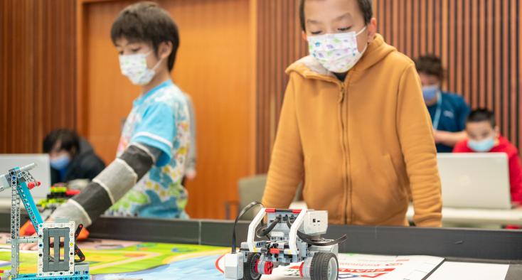 boy with black hair standing at a table with a robot