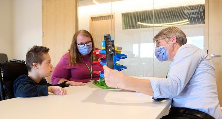 Two adults playing a toy with a child who is sitting on a wheelchair