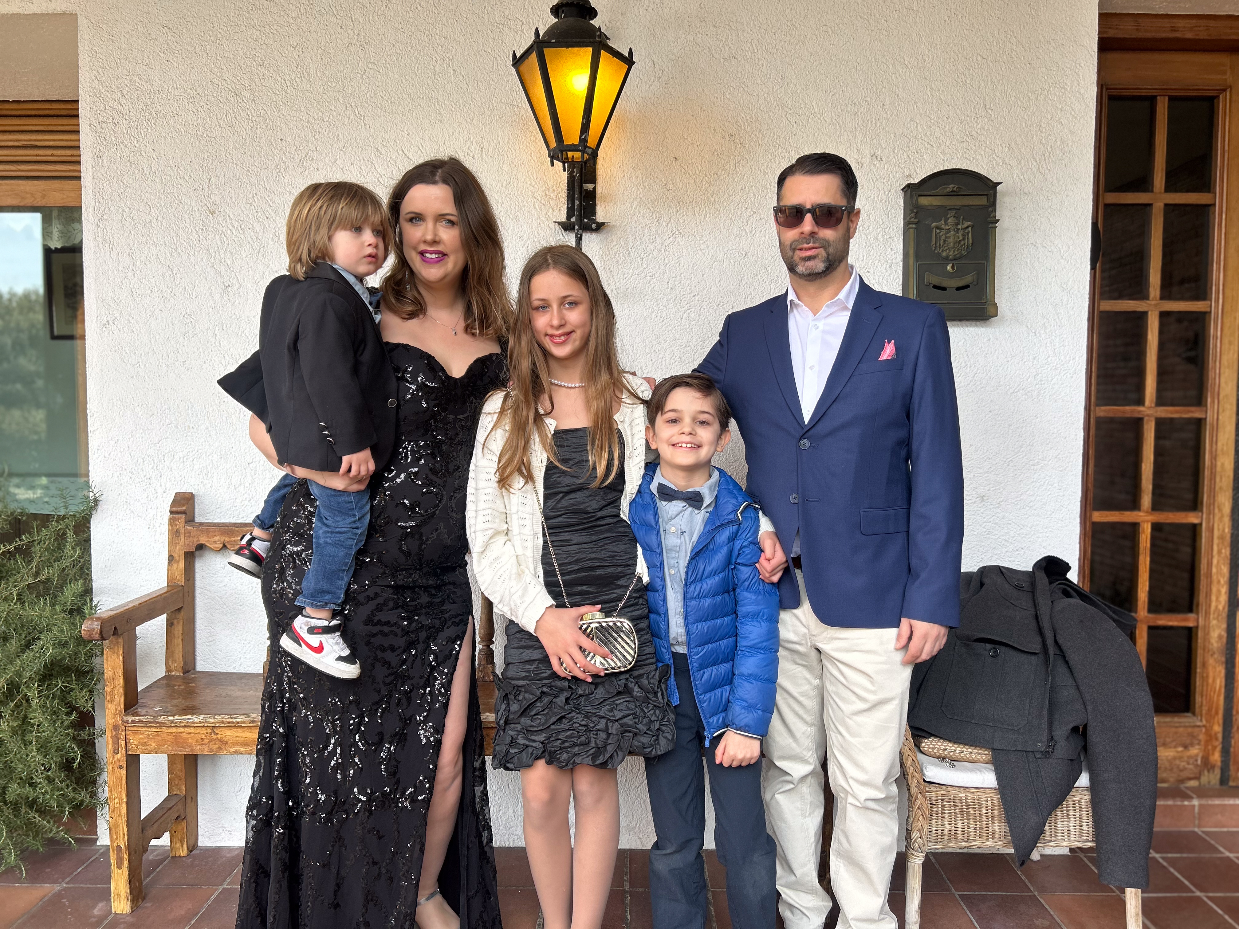 A family of five stands in front of a house wearing formal wear