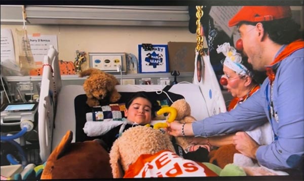 A child on a hospital bed with two clowns standing by the side