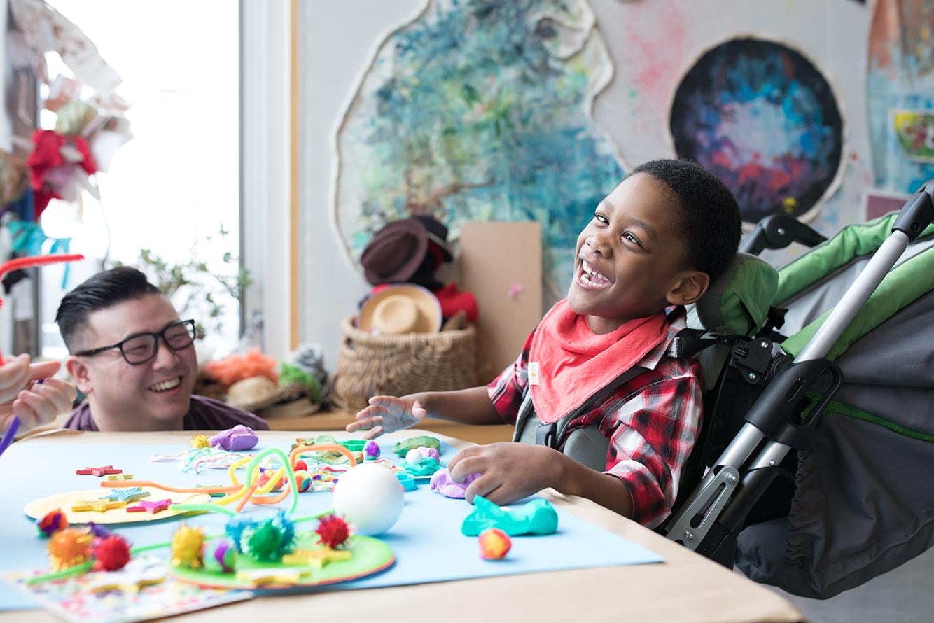 A little boy in a wheel chair playing with arts and crafts at a table