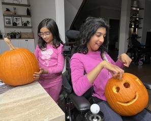 Two girls with pink shirts carve pumpkins