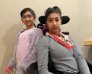 Teen with dark hair and red scarf in wheelchair beside girl with dark hair and pink shirt