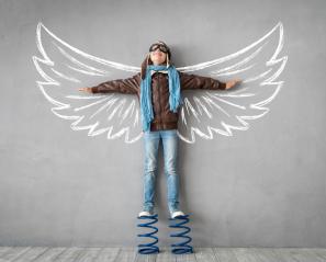 Boy stands on springs with arms spread on wall image of wings