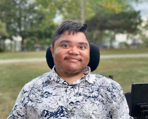 Man with dark hair in wheelchair smiles in park