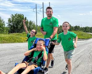 A dad and three children run together outdoors using an adapted stroller