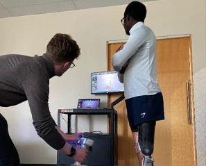 Left: Two people are testing something through a computer monitor; right: some leaflets and pens on the table.