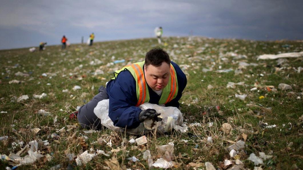 Young man with Down syndrome lying in field of garbage picking up trash