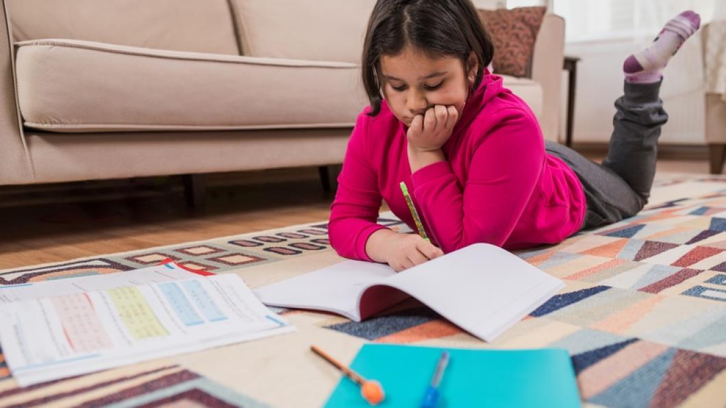 Girl lying on living room floor surrounded with school work